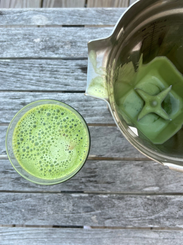 A glass of vibrant green matcha rests on a wooden table beside an empty blender, ready for your daily glow ritual.