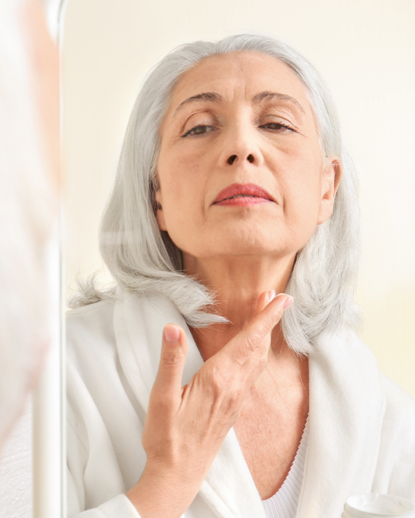 A Older woman with silver hair checking her neck and décolletage.