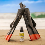 Raw Elements SPF 50 mineral sunscreen spray standing on sand with snorkeling fins