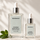 Two bottles of Peppermint Magnesium Oil with fresh mint leaves in a glass bottle one is 3.4fl oz and the other is 1 oz - both travel friendly 