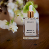 Behrhaus Magnesium Oil in a clear glass dropper bottle displayed on a wooden table with soft white flowers and warm natural lighting.
