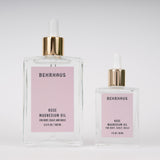 two clear glass bottles  of Behrhaus rose magnesium oil on white background, one larger 3.4fl oz botlle and one smaller 1 fl oz bottle, both with soft pink labels and gold dropper caps