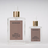 Two clear glass bottles  of Behrhaus. Vanilla magnesium oil on white background, one larger 3.4fl oz botlle and one smaller 1 fl oz bottle, both with soft brown labels and gold dropper caps